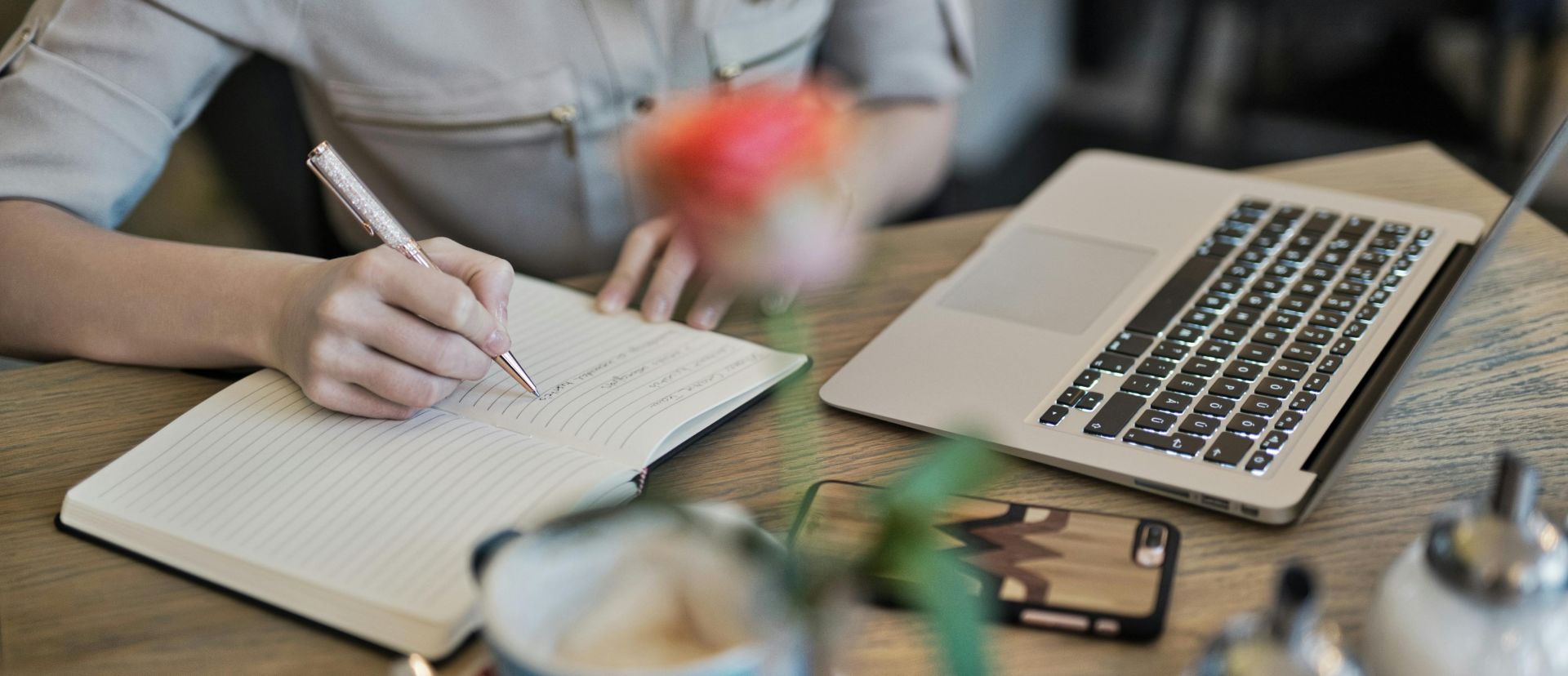 Person Writing On A Notebook Beside Macbook